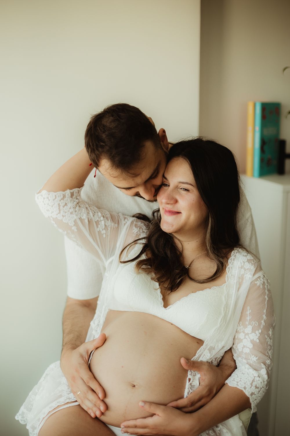 Couple embracing during maternity photo shoot, man kissing pregnant woman's head while holding her baby bump.