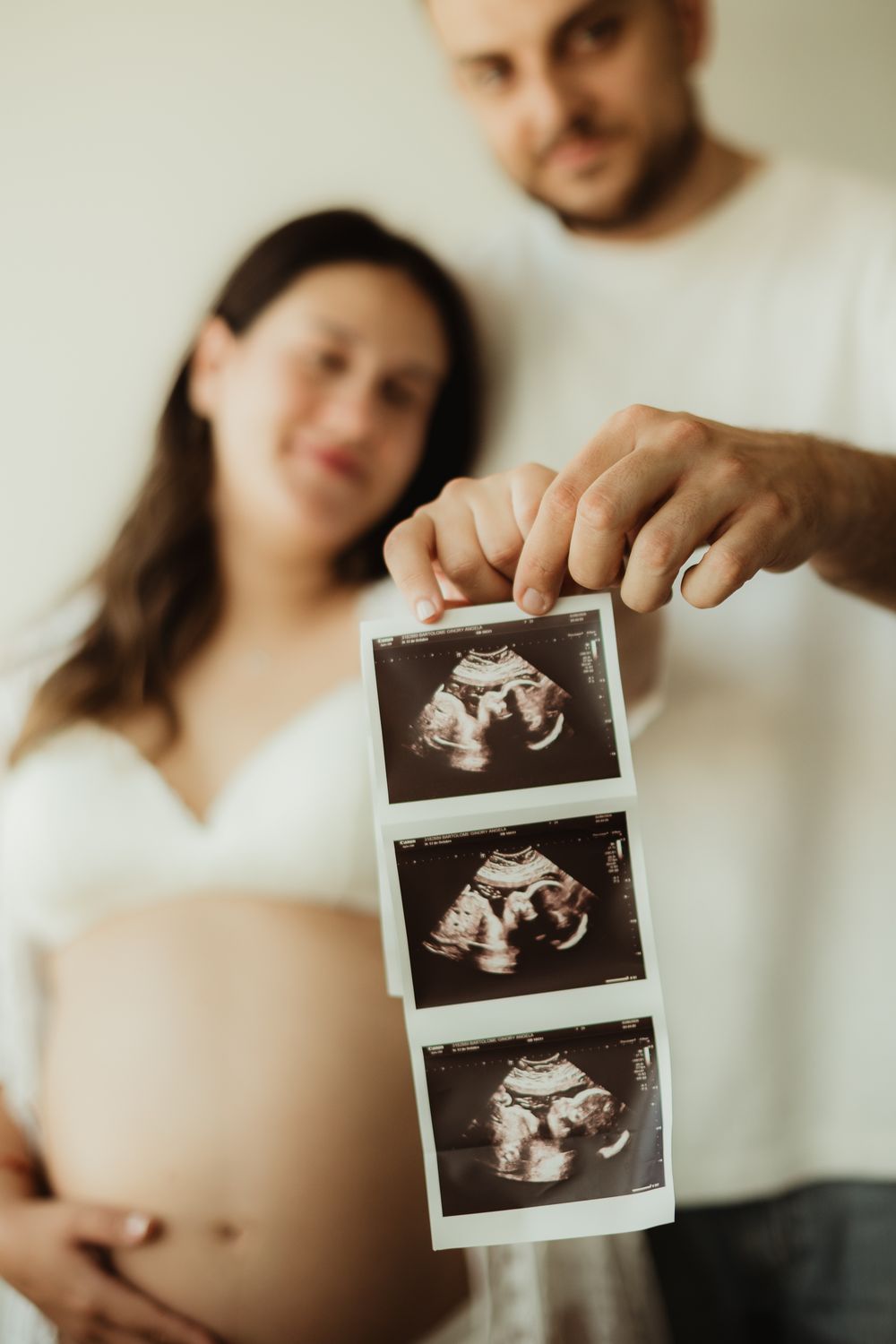 Pregnant couple holding ultrasound sonogram photos, showing baby scan images while woman displays bare baby bump.