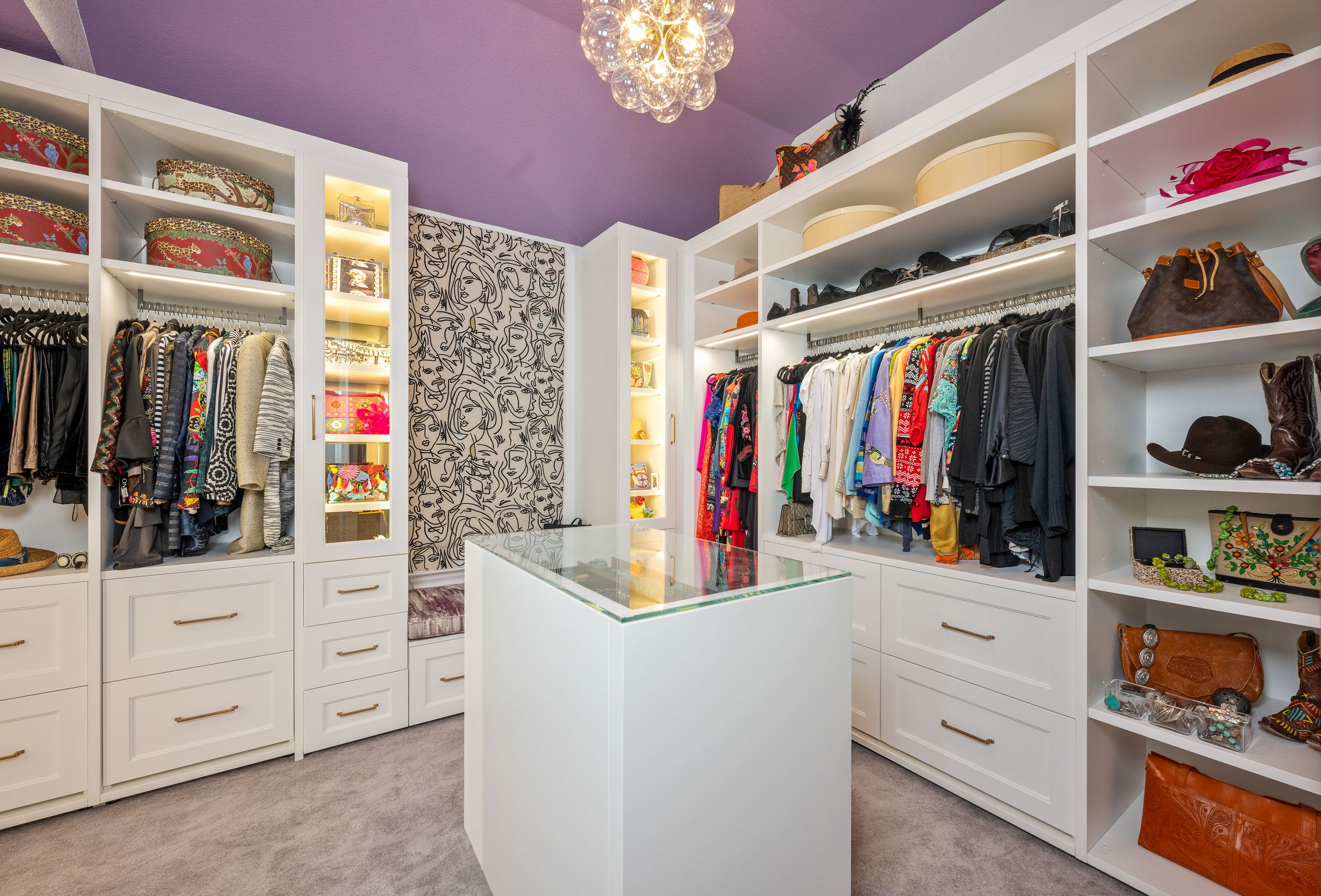 Large walk-in closet with white built-in shelving, center island, purple ceiling, and chandelier lighting.