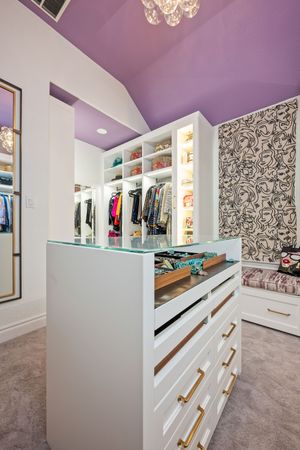 Spacious walk-in closet with purple ceiling, white built-ins, center island with glass top, and patterned wallpaper.