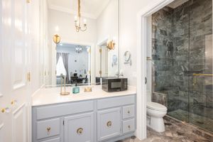 Gray double vanity bathroom with gold fixtures, marble floors, large mirror, and glass shower enclosure.