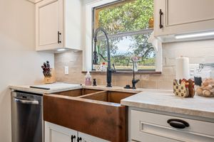 Kitchen with copper farmhouse sink, black faucet, cream cabinets, and beige tile backsplash with garden view.