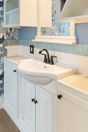 White bathroom vanity with pedestal sink, black hardware, blue floral wallpaper, and subway tile backsplash.
