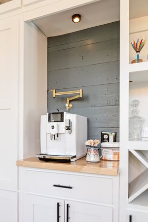 Built-in white coffee bar niche with espresso machine, gold pot filler, and shiplap accent wall.