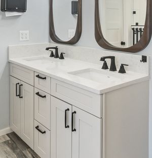 White double sink vanity with quartz countertop, black hardware, and oval wood-framed mirrors.