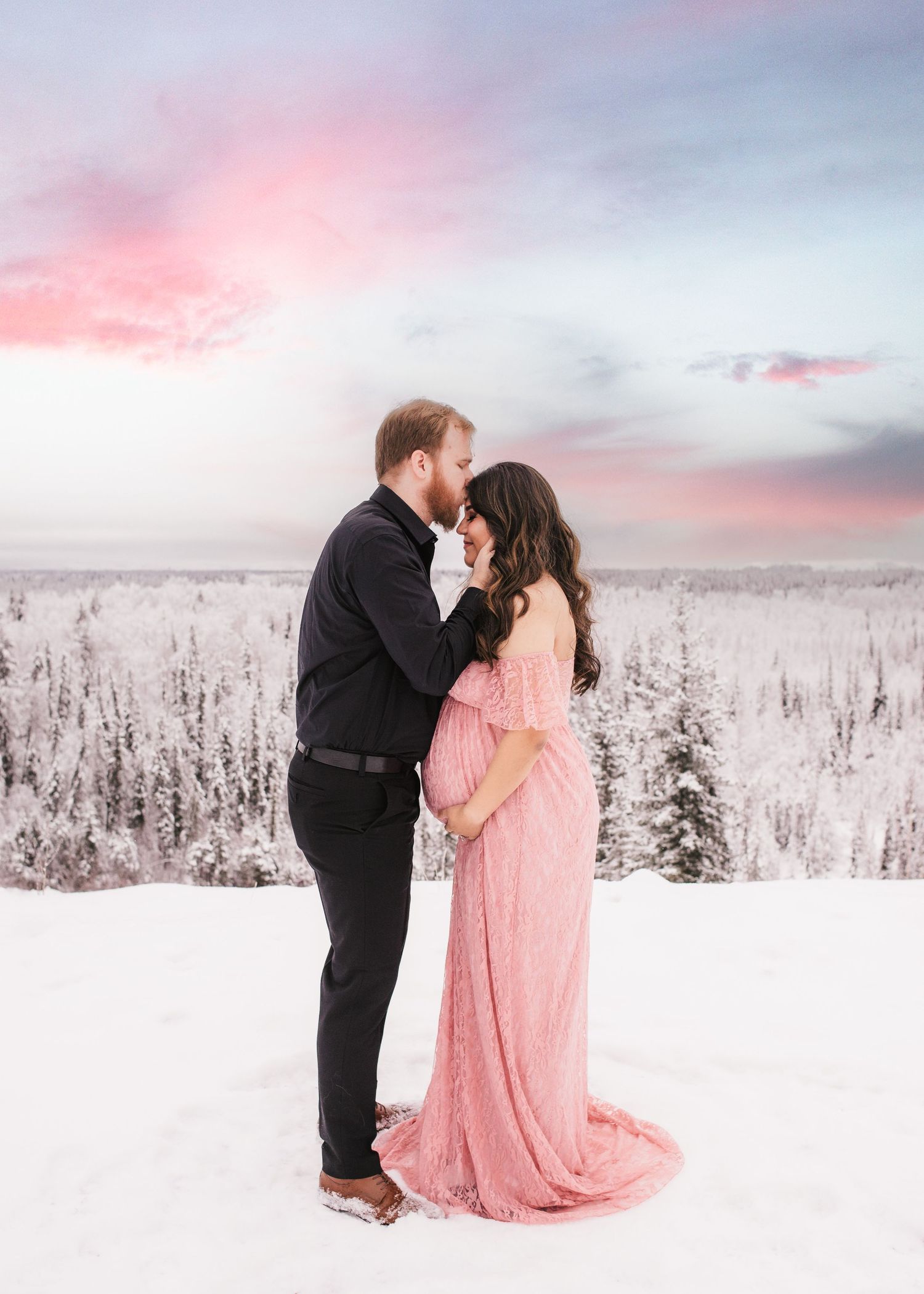 Expecting couple embracing in a snowy winter landscape during a maternity session