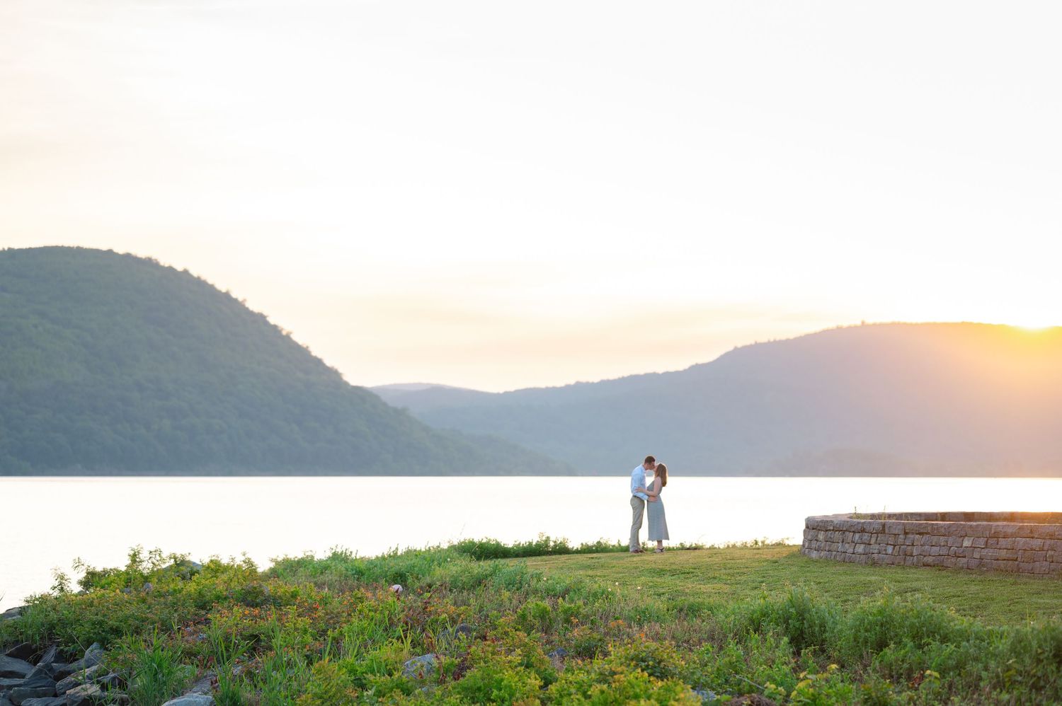 Couple embracing at sunset in Peekskill Landing Park in Westchester during a proposal with the sunset light and Hudson Valley behind them.