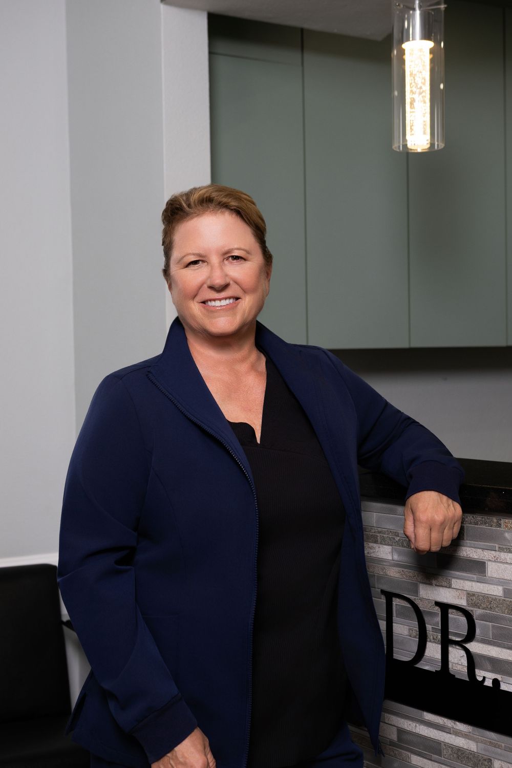 Professional woman in navy blazer smiling confidently in a modern office reception area.