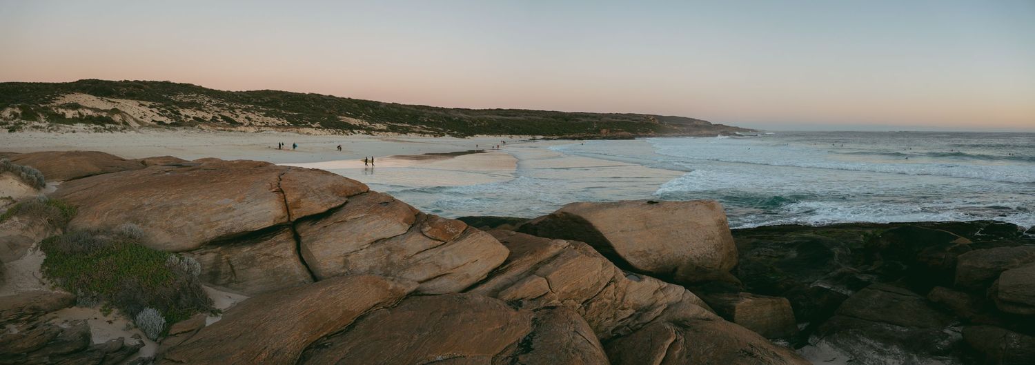 Rocky shoreline and turquoise ocean meet a sandy stretch of Redgate Beach beneath a soft pastel sky.
