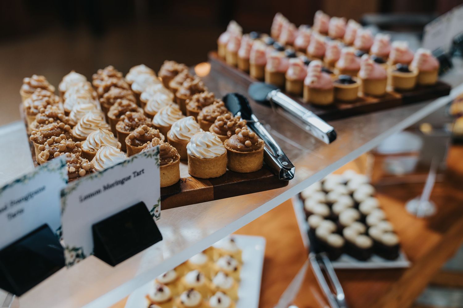 Elegant dessert table display with rows of cupcakes, tarts, and petit fours at a catered event.