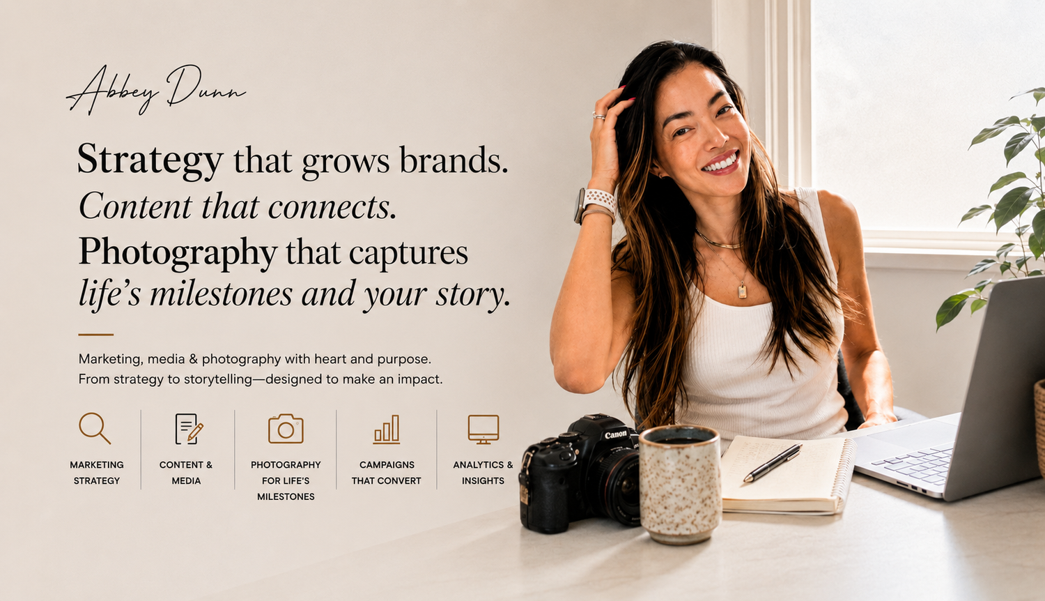 A smiling woman sits at a desk with a camera, laptop, and notebook, representing a marketing and media strategy brand.