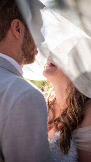 Bride and groom share an intimate moment under a flowing white veil on their wedding day.