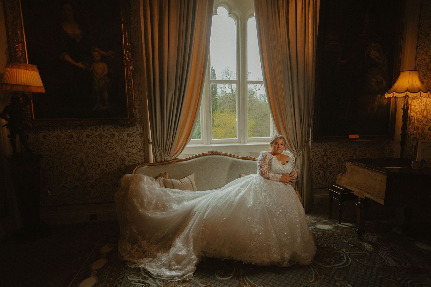 Bride in elegant white ball gown seated on chaise lounge by draped window in Cabra Castle, Co. Cavan