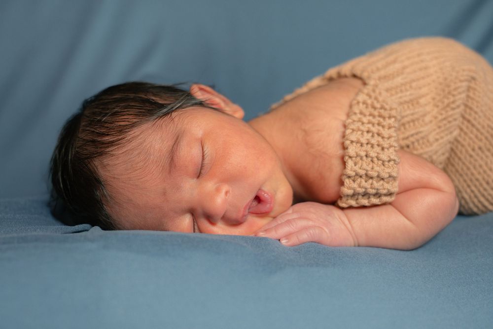 Peaceful newborn baby sleeping in a knit tan outfit on a soft blue blanket.