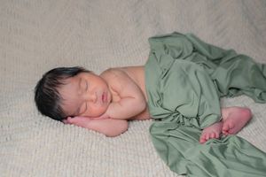 Peaceful newborn baby sleeping on a soft white blanket wrapped in a green cloth.