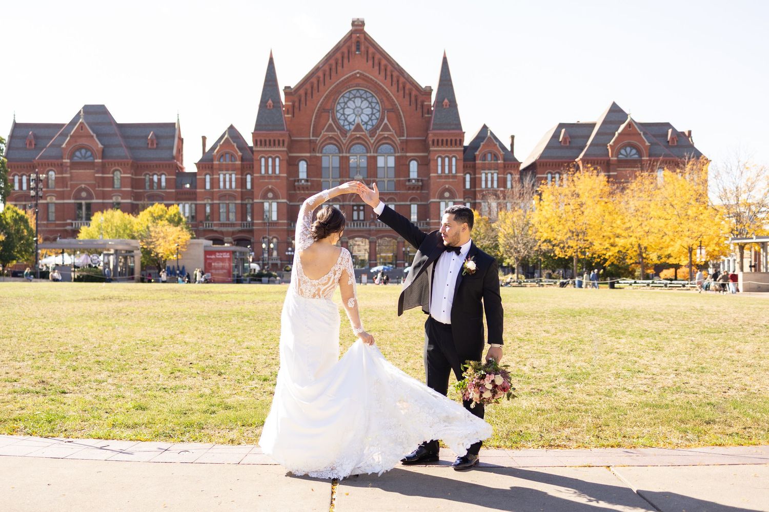 A couple in wedding attire shares joyful moments outdoors with their brown labrador retriever dog.