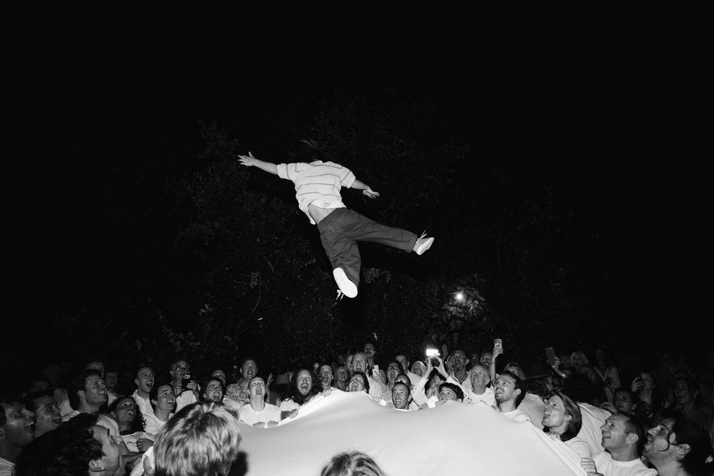 Black and white photo of a person crowd surfing at an outdoor concert, soaring above a large crowd at night.