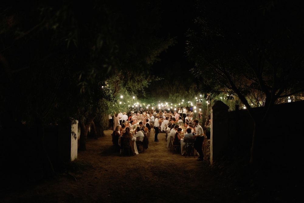 Outdoor evening wedding reception under string lights surrounded by trees at night.