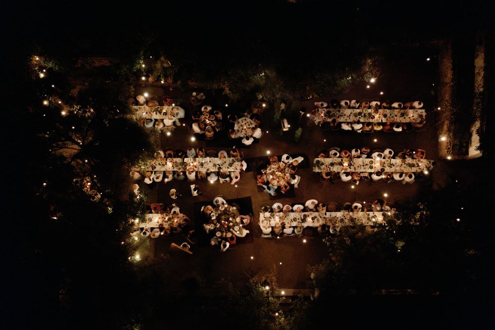 Aerial night view of elegantly lit wedding reception tables arranged outdoors with warm glowing lights.