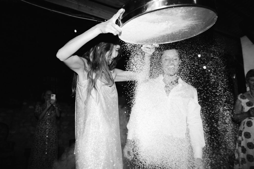Black and white photo of a woman pouring a bucket of water over a man at a festive outdoor celebration.