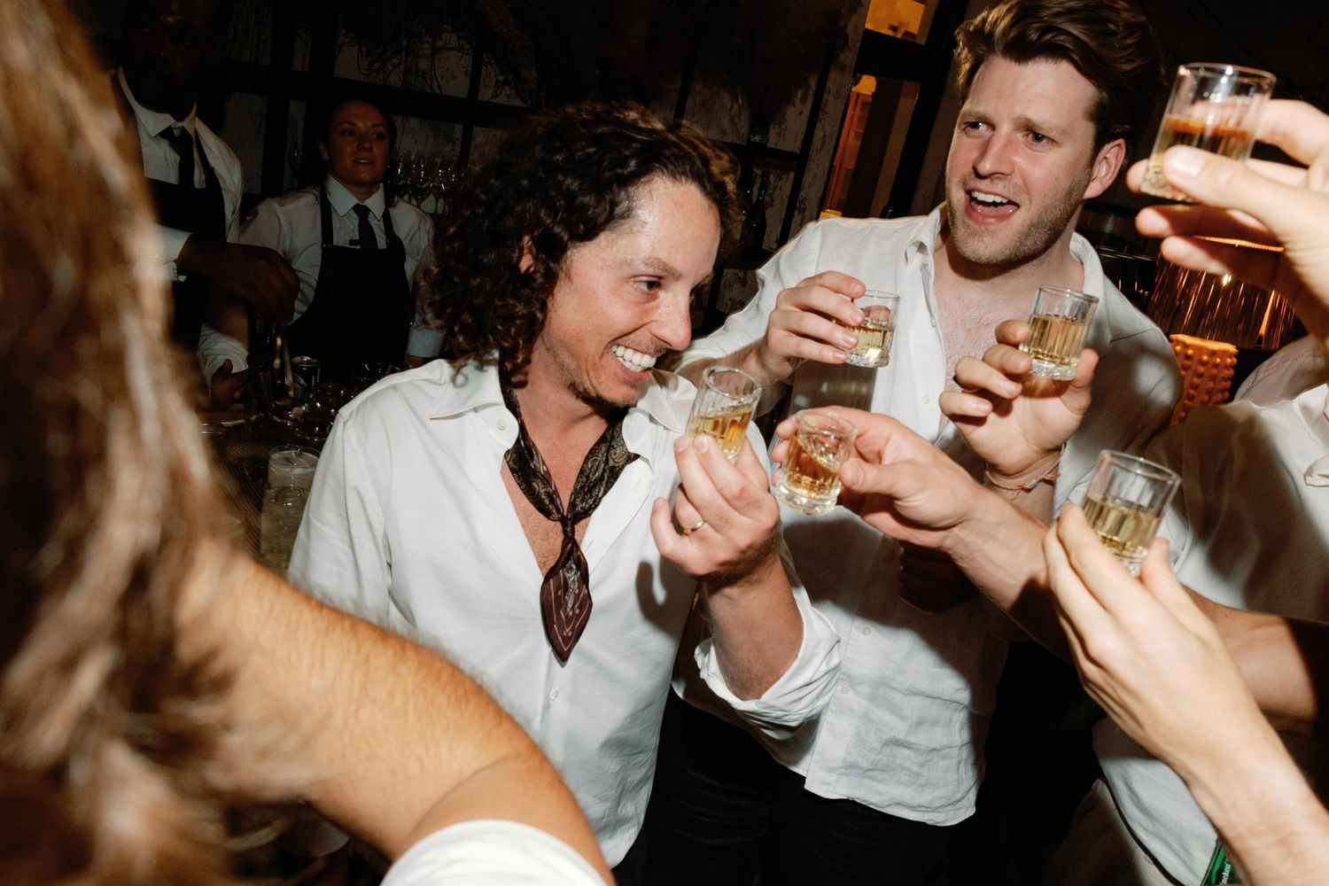 Wedding guests laugh and clink glasses together in celebratory toast at reception party.