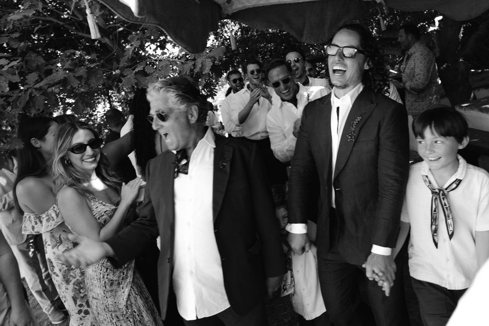Black and white photo of elegantly dressed guests laughing and socializing at an outdoor wedding reception.