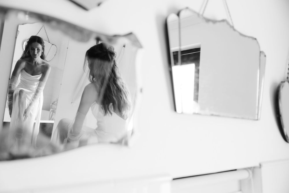 Black and white reflection of a bride in a wedding dress captured in vintage mirrors on a dresser.