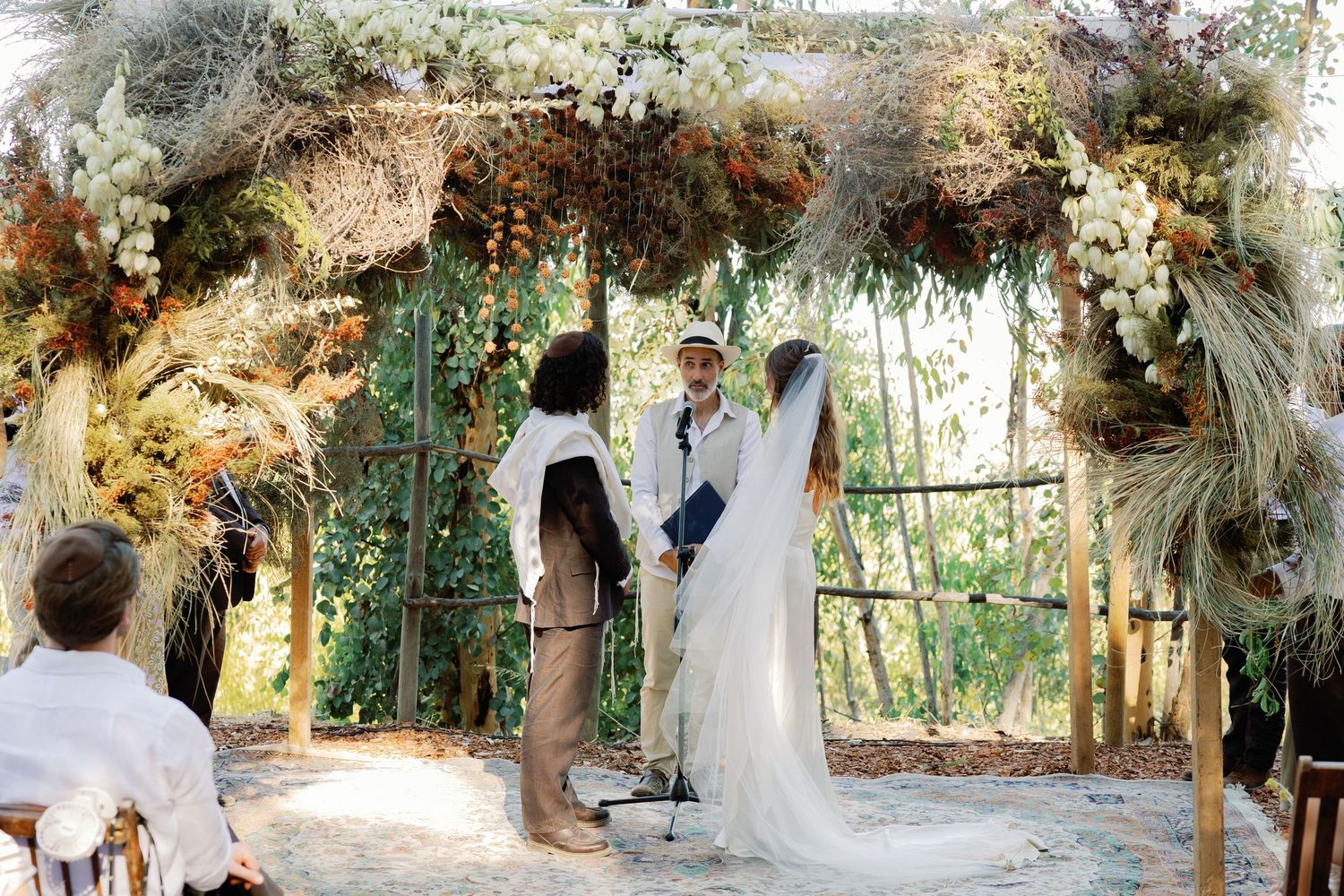 Bride and groom exchange vows under rustic floral arch adorned with dried flowers at outdoor wedding.