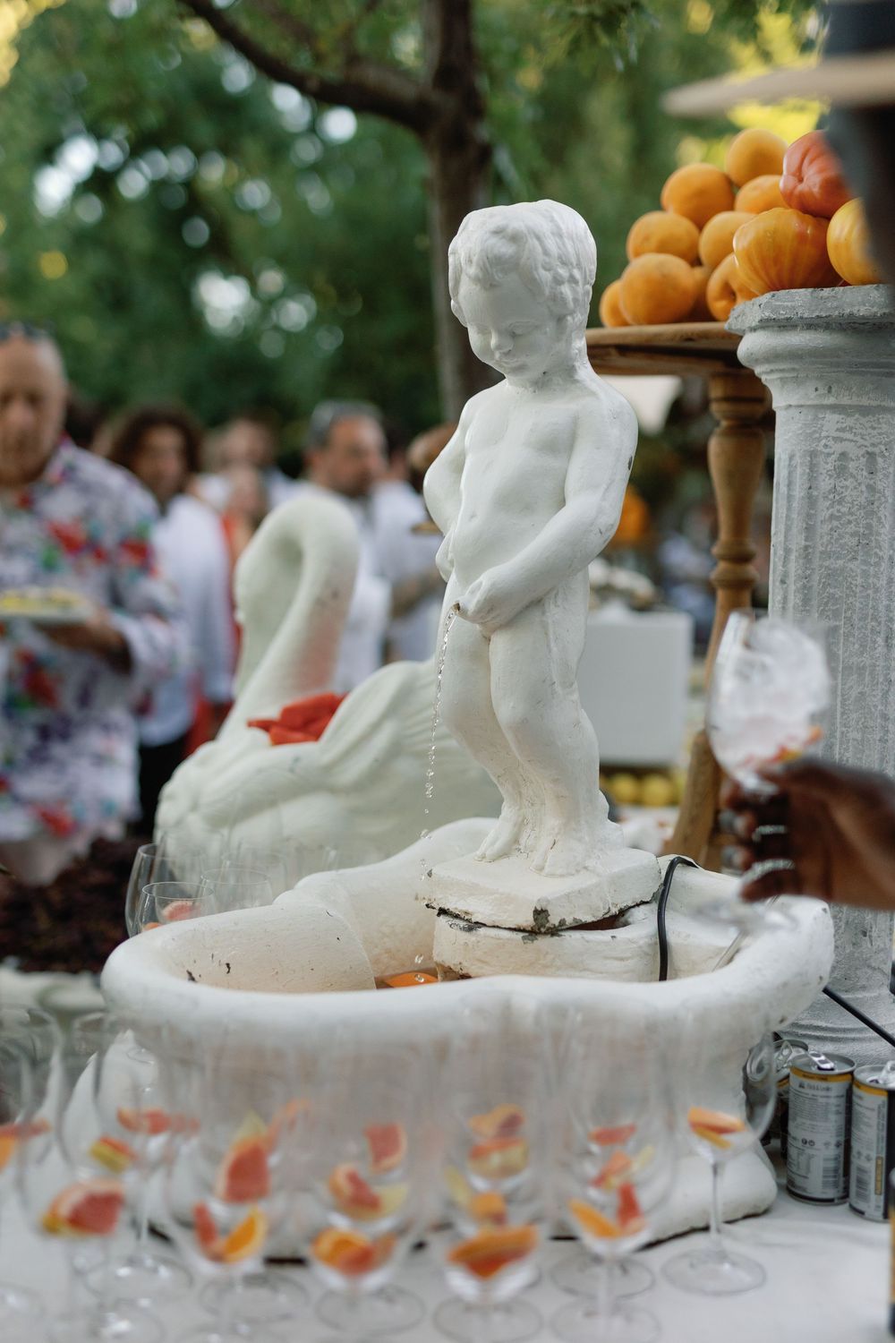 White cherub fountain centerpiece surrounded by champagne glasses and fresh fruit at an outdoor wedding reception.