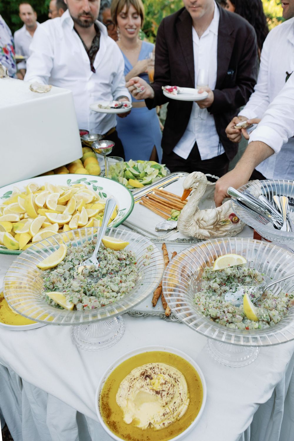 An elegant outdoor wedding reception buffet table featuring seafood, salads, lemon slices, and hummus.