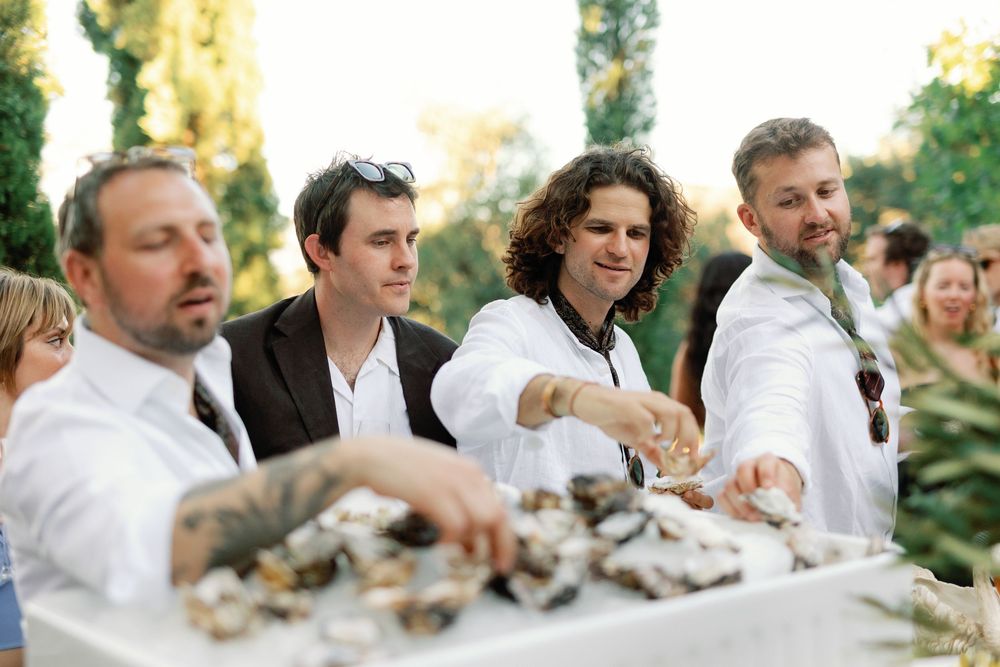 Wedding guests gathered around oyster bar at outdoor garden wedding cocktail reception.