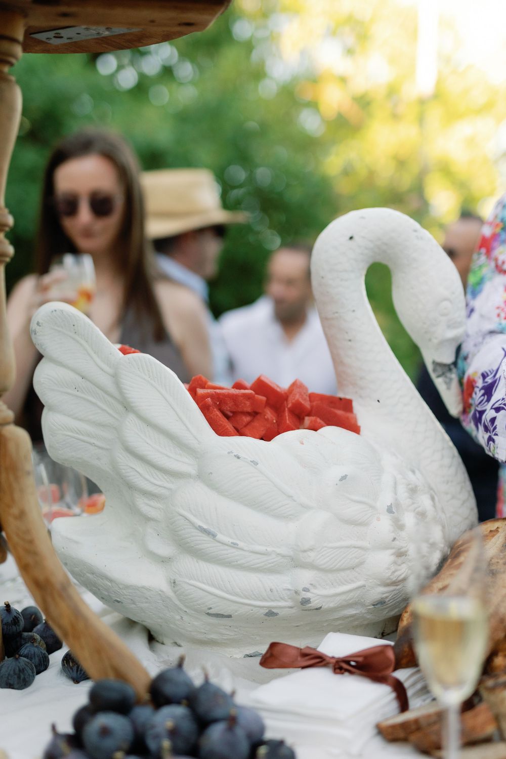 Elegant white swan sculpture filled with fresh watermelon slices on outdoor wedding reception table.