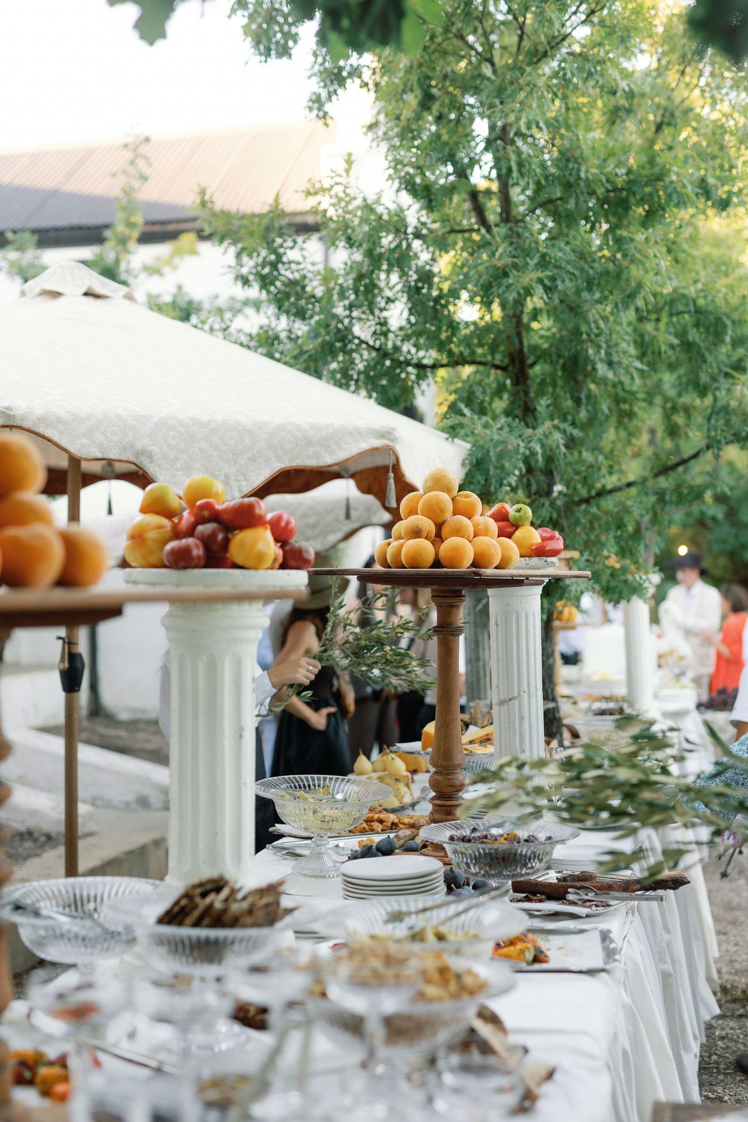 Elegant outdoor wedding buffet table with white columns displaying fresh fruit bowls and crystal dishes.