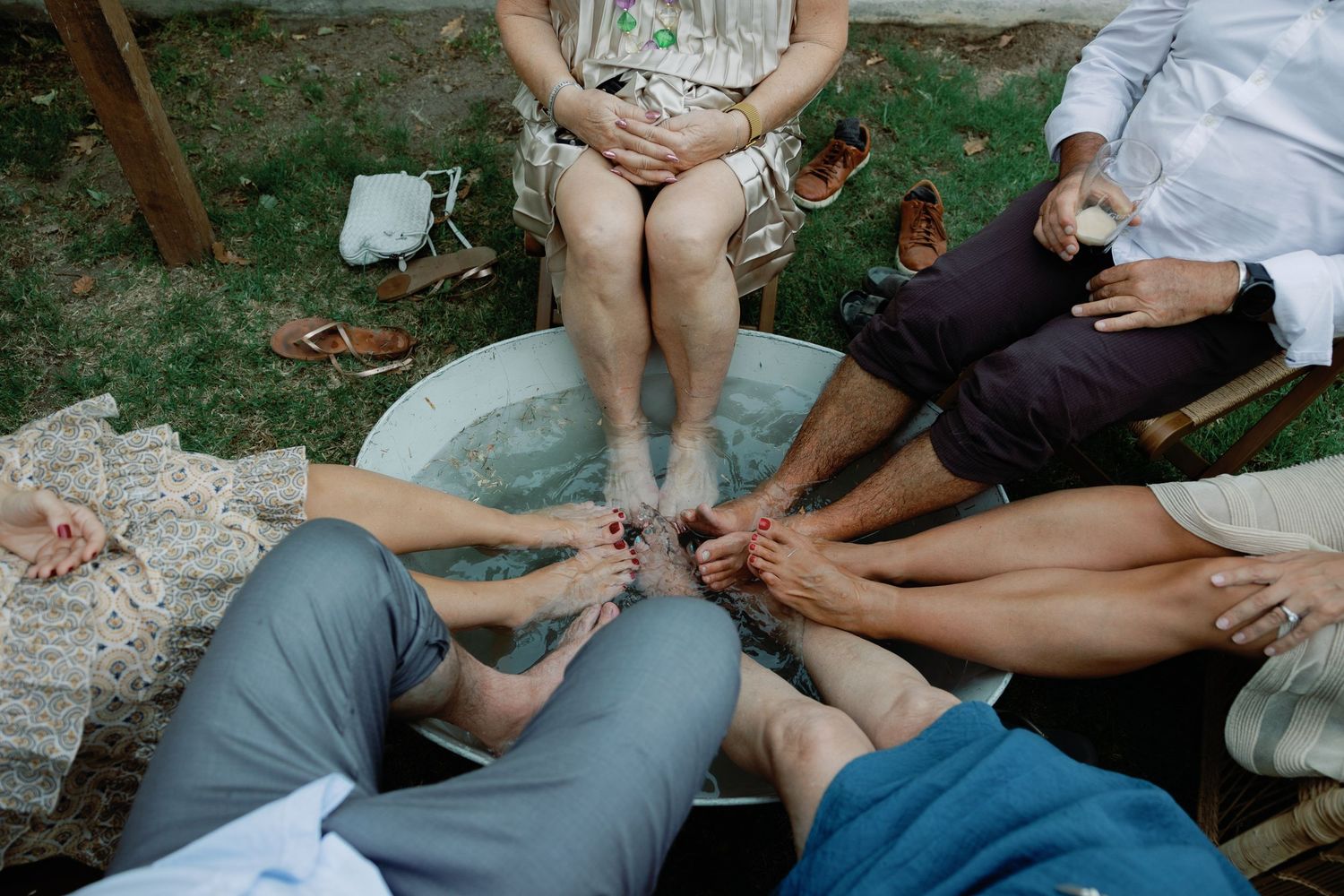 Wedding guests soaking their feet together in a large basin of water during an outdoor celebration.