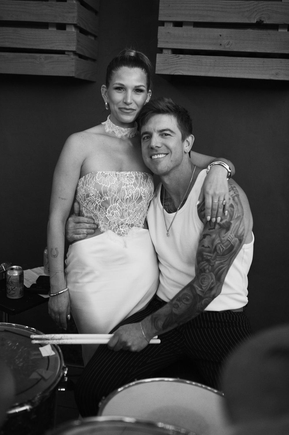 Black and white photo of a smiling couple posing together, man with tattoos wearing tank top, woman in strapless lace top.
