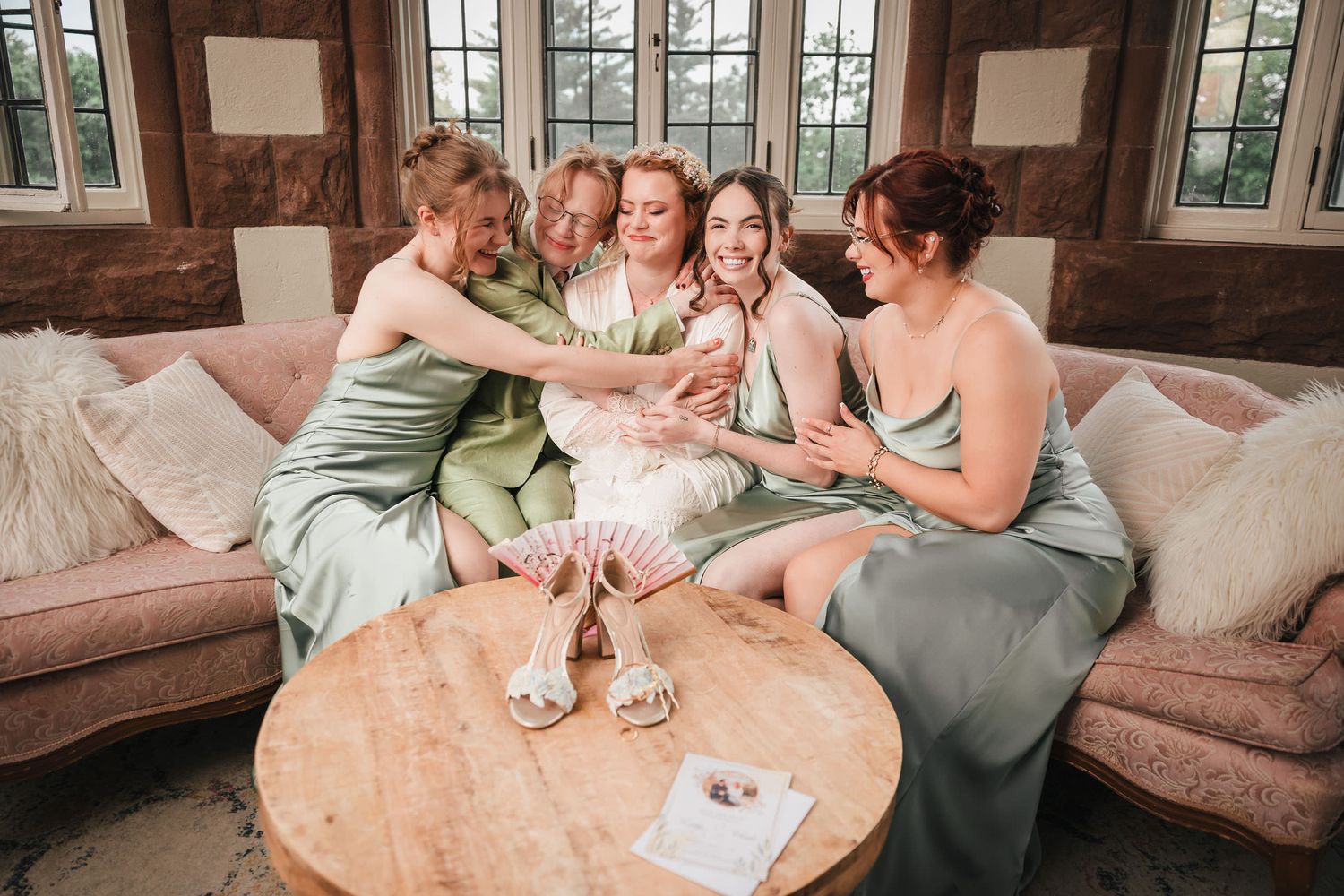 Bride surrounded by her closest bridesmaids and her brother, all laughing together on a couch at Searles Castle.