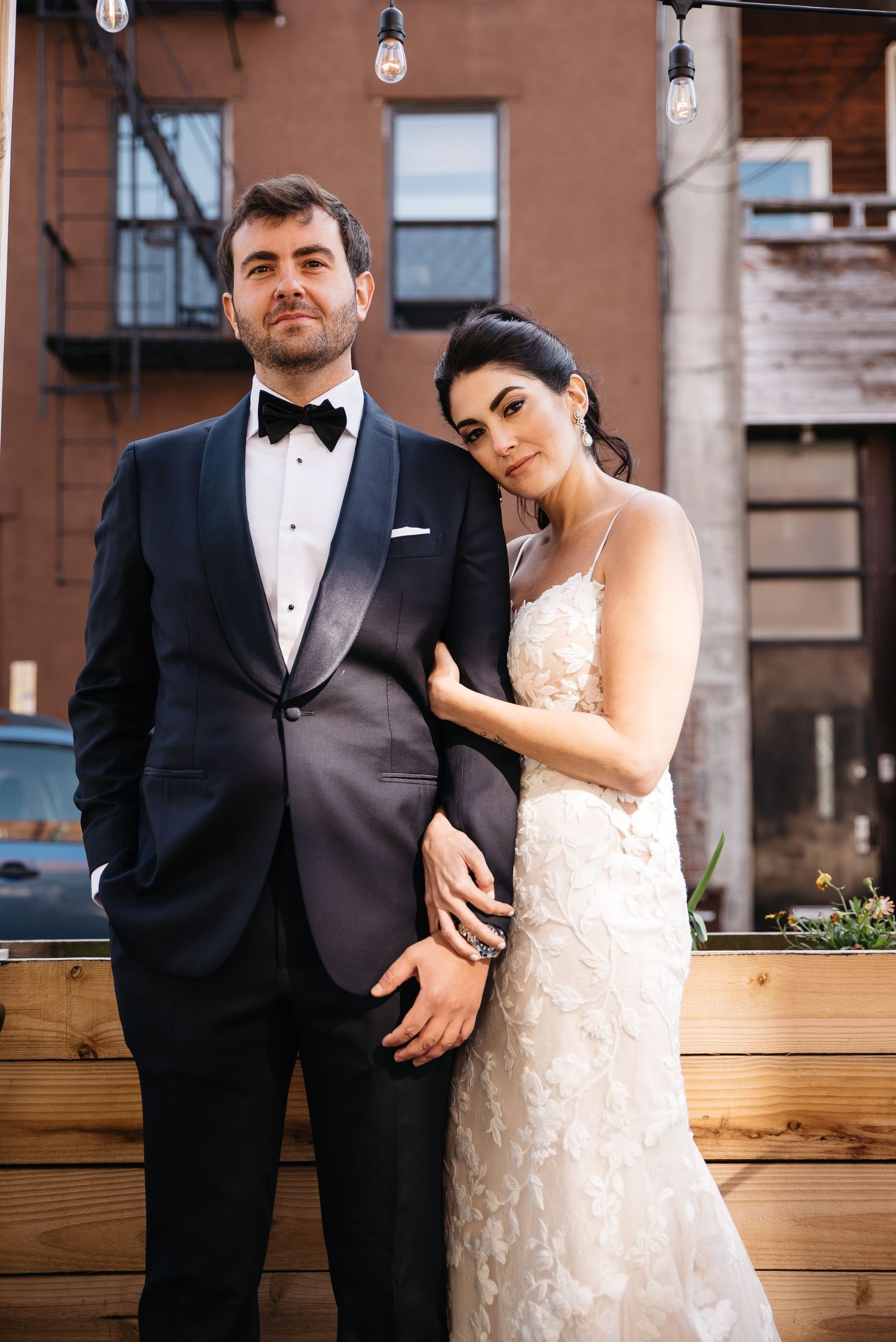 A newlywed couple poses against an urban brick building backdrop.