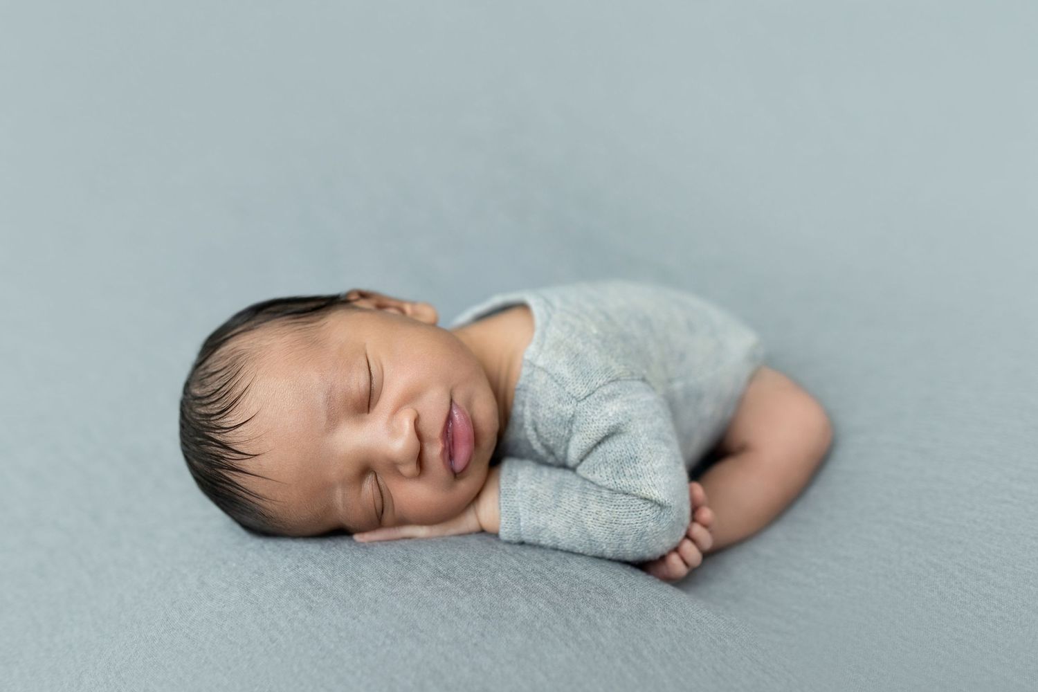 Peaceful newborn baby sleeping on a soft blue-gray blanket wearing a light gray onesie.