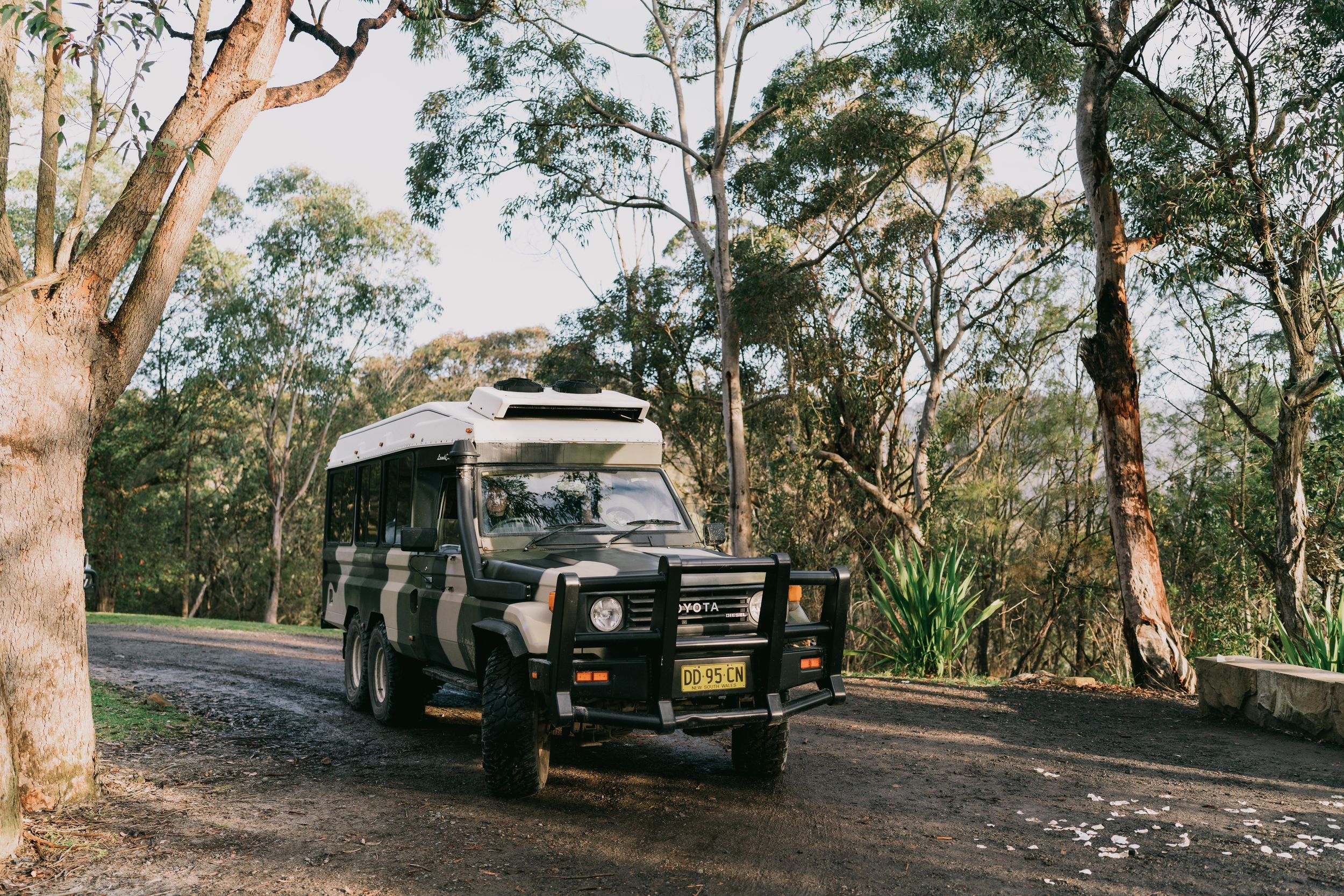 A rugged 4WD vehicle parked on a dirt road surrounded by Australian bush and eucalyptus trees.