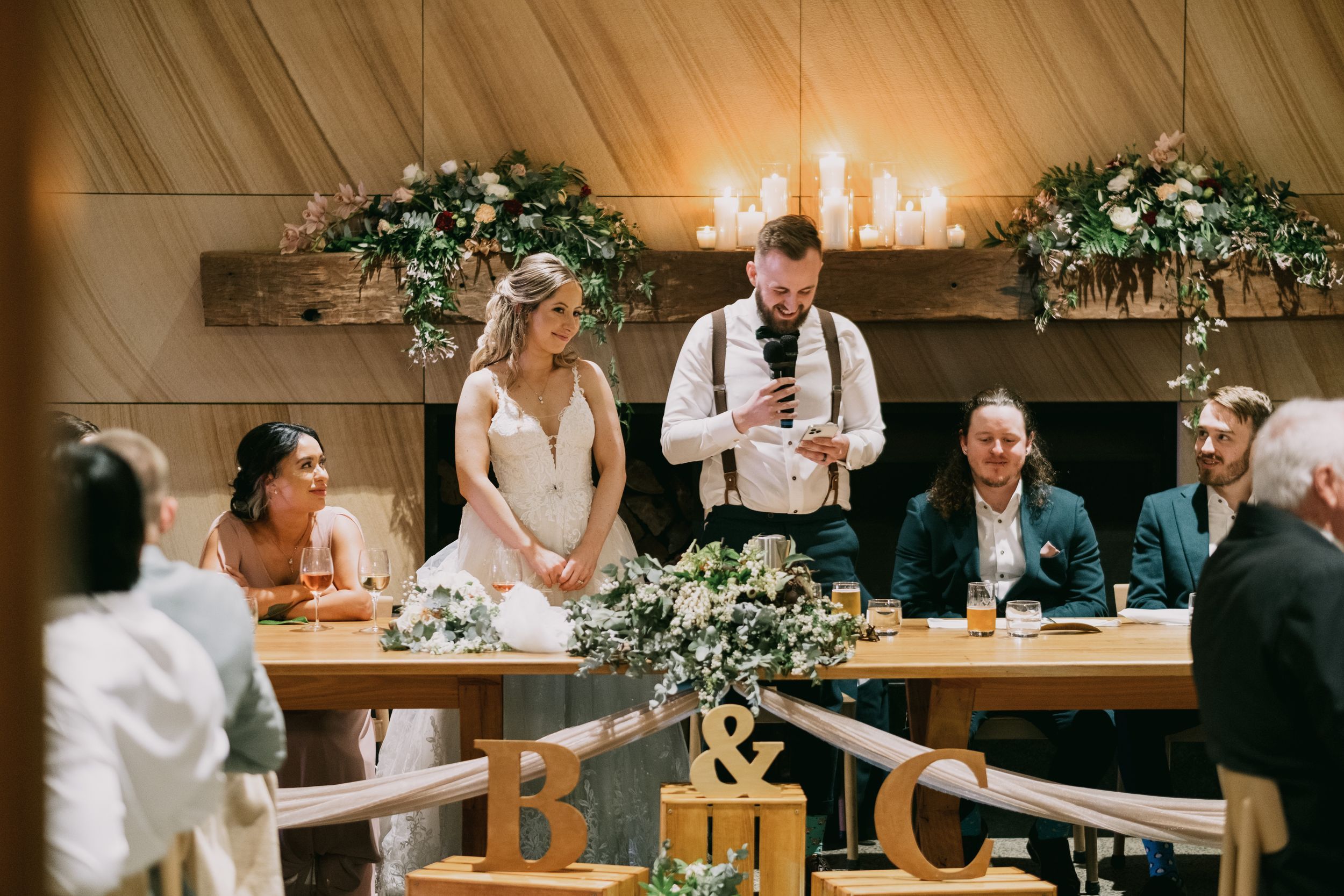 Bride and groom laugh together at the bridal table decorated with greenery and monogram letters.