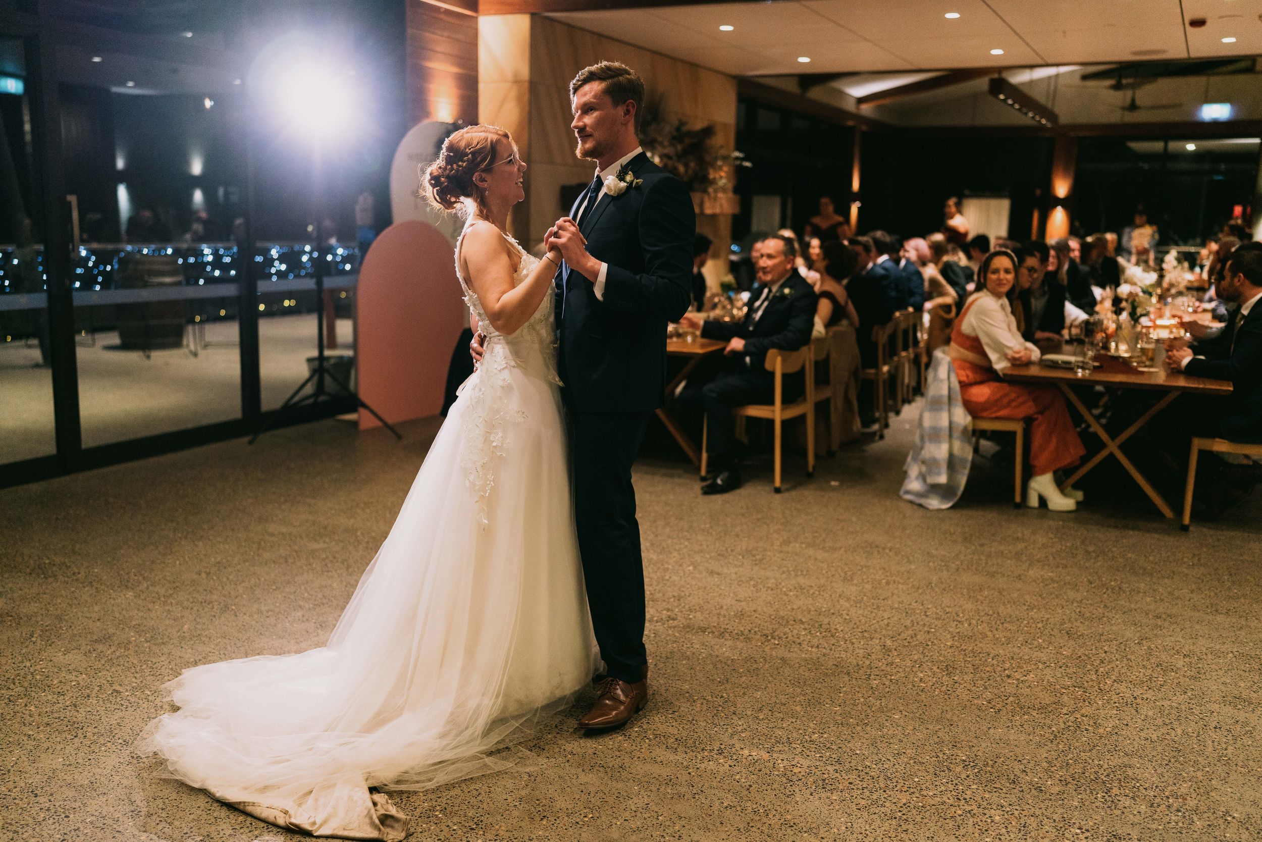 Bride and groom share their first dance at an elegant indoor wedding reception venue at night.