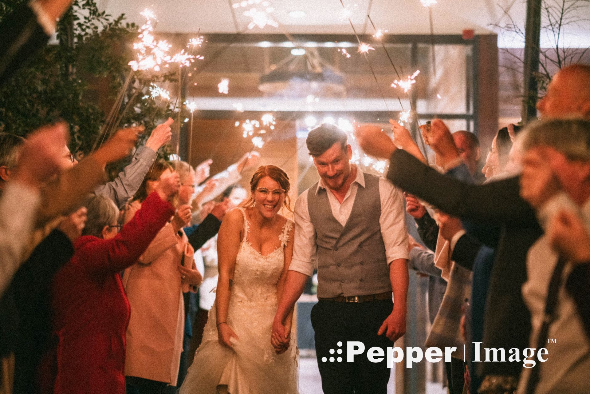 Bride and groom walk through a sparkler tunnel surrounded by cheering guests at night.