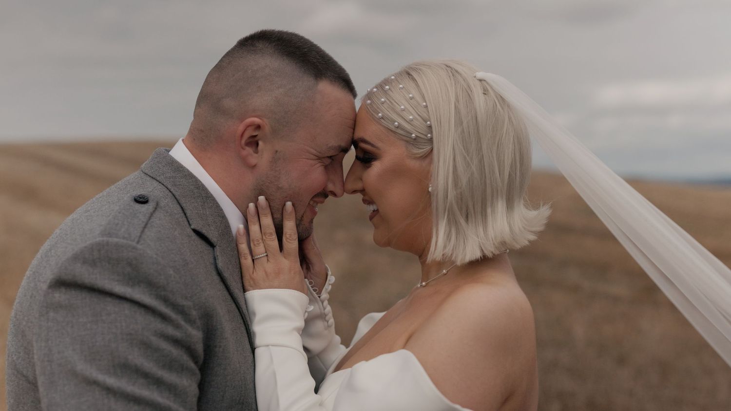 Bride and groom holding each other, forehead to forehead in a golden field within Dumfries and Galloway Scotland