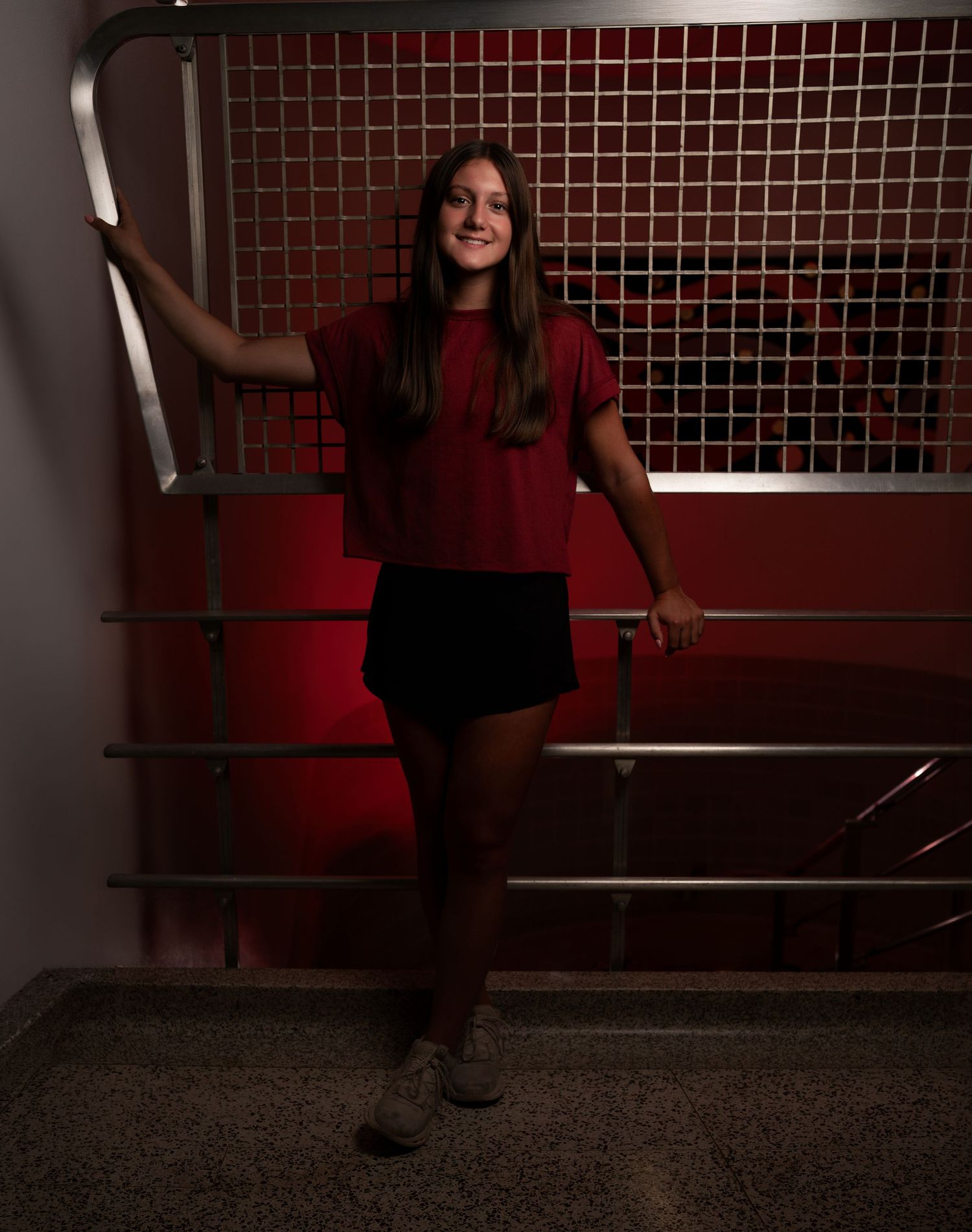 Dramatic senior portrait of a girl in a red top photographed in an urban stairwell