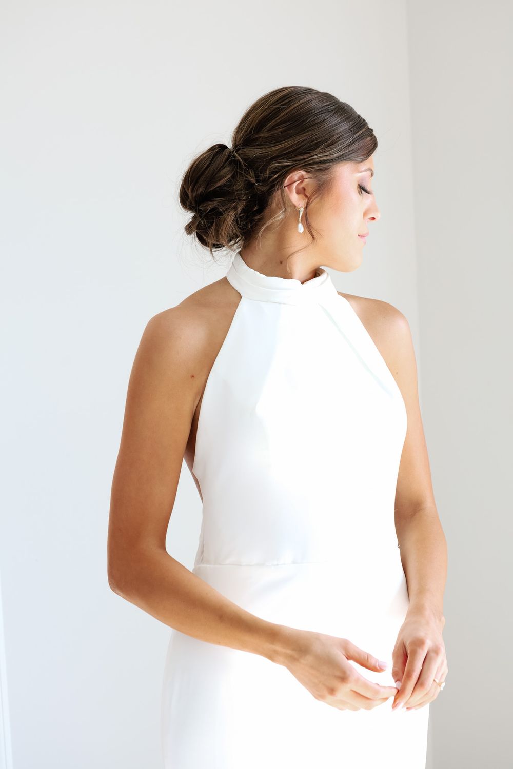 Elegant bride in a white halter neck wedding gown with an updo hairstyle and pearl earrings.
