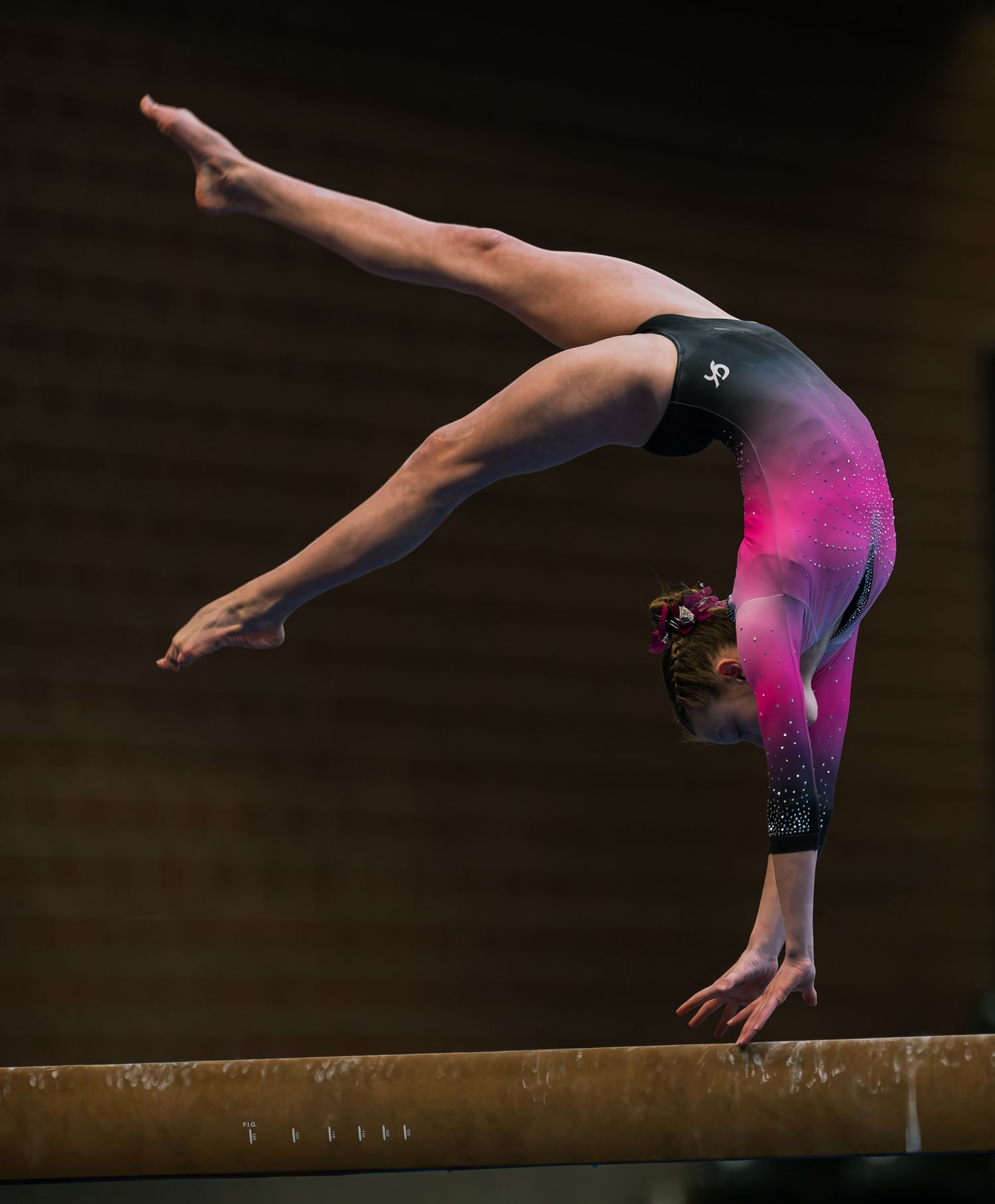 Gymnast performing a back walkover on a balance beam wearing a pink and black sparkly leotard.