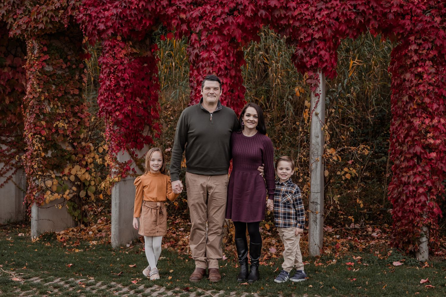 Family standing together among the red autumn trees at Maximapark in Utrecht for a fall photoshoot in the Netherlands