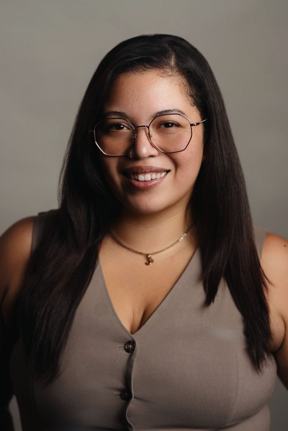 Professional headshot of a smiling young Asian man in a plaid shirt on a gray background.