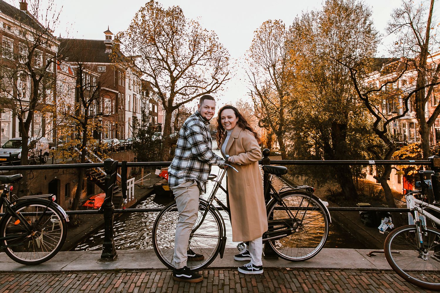 Tourist couple posing with bicycles on a canal bridge in Utrecht city during an autumn photoshoot.