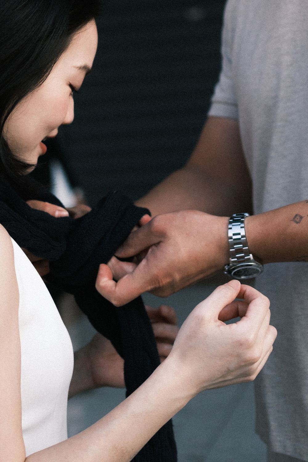 A woman wrapping black hand wraps assisted by a person wearing a silver watch and gray shirt.